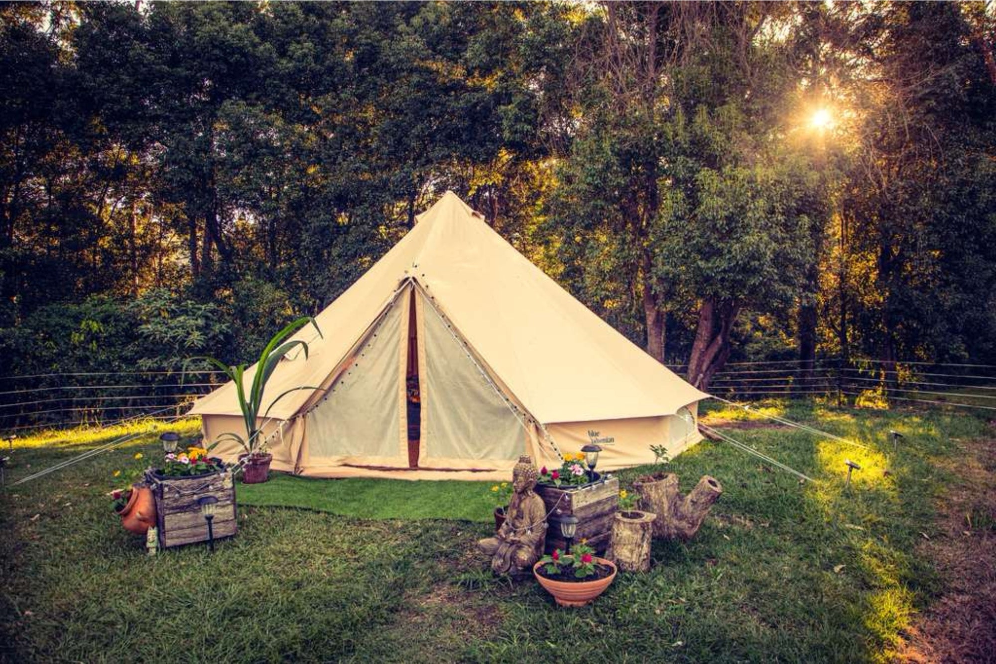 6m canvas bell tent set up in a garden for glamping with decorative plants and outdoor seating