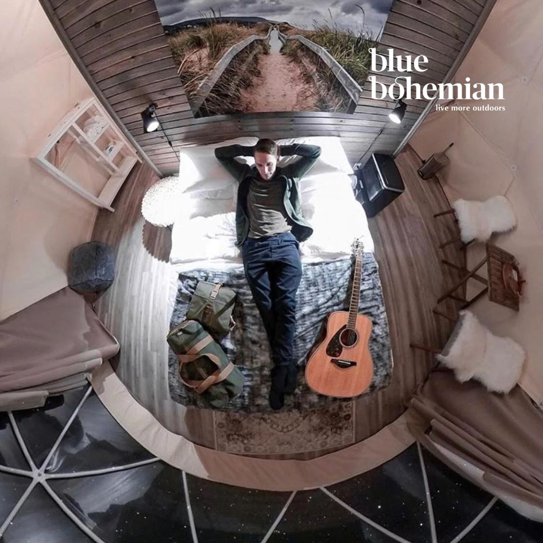 Person lying on a bed with a guitar, surrounded by cozy decor in a goedesic dome